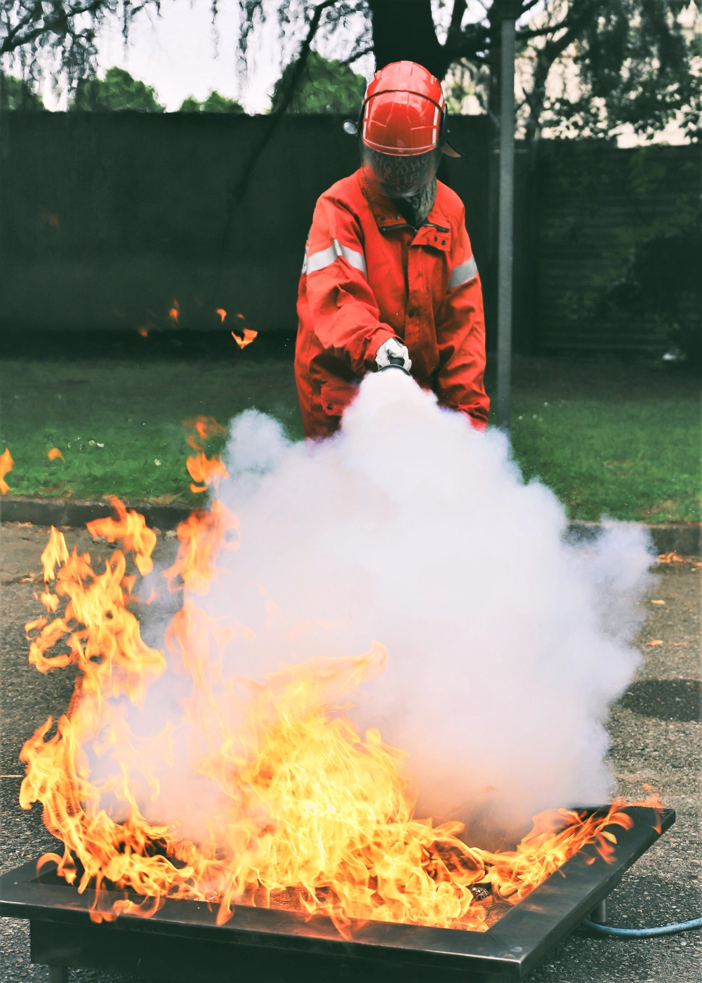 Pracownik w stroju ochronnym gaśnie ognisko przy użyciu gaśnicy chemicznej podczas szkolenia przeciwpożarowego