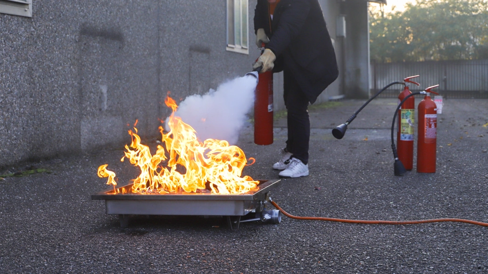 Instruktor gaszący ognisko w metalowej palenisku przenośną gaśnicą podczas szkolenia przeciwpożarowego