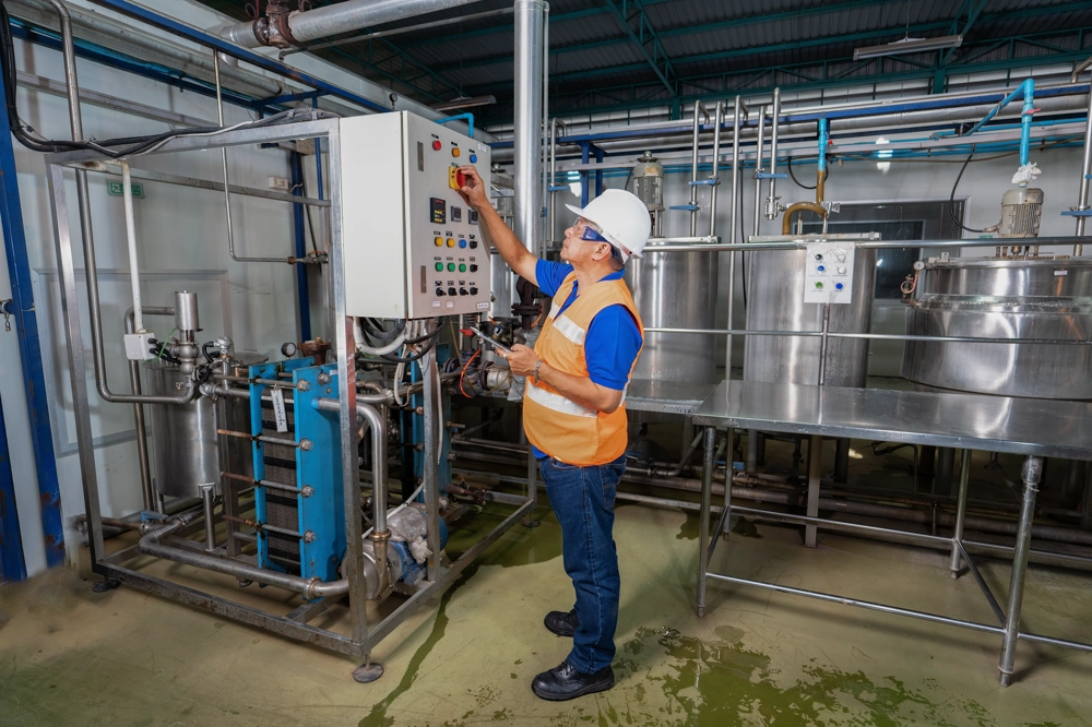 Pracownik w kasku i kamizelce kontroluje panel maszyn w hali produkcyjnej – Nadzór bhp