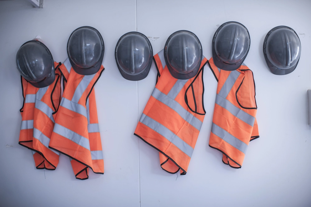 Szare kaski i pomarańczowe kamizelki odblaskowe wiszące na ścianie przygotowane do szkolenia bhp dla pracowników